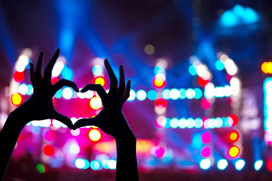 Someone makes a heart with their hands at a large concert. Likely a Taylor Swift concert.