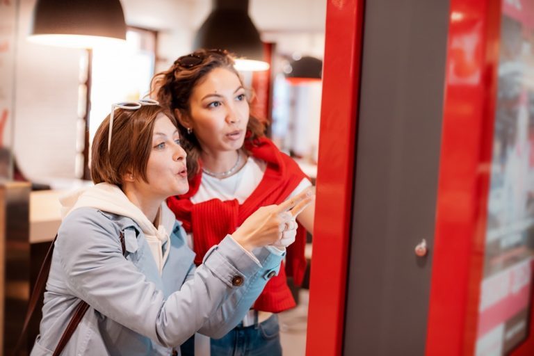 Two young women browsing on a self-service kiosk machine.